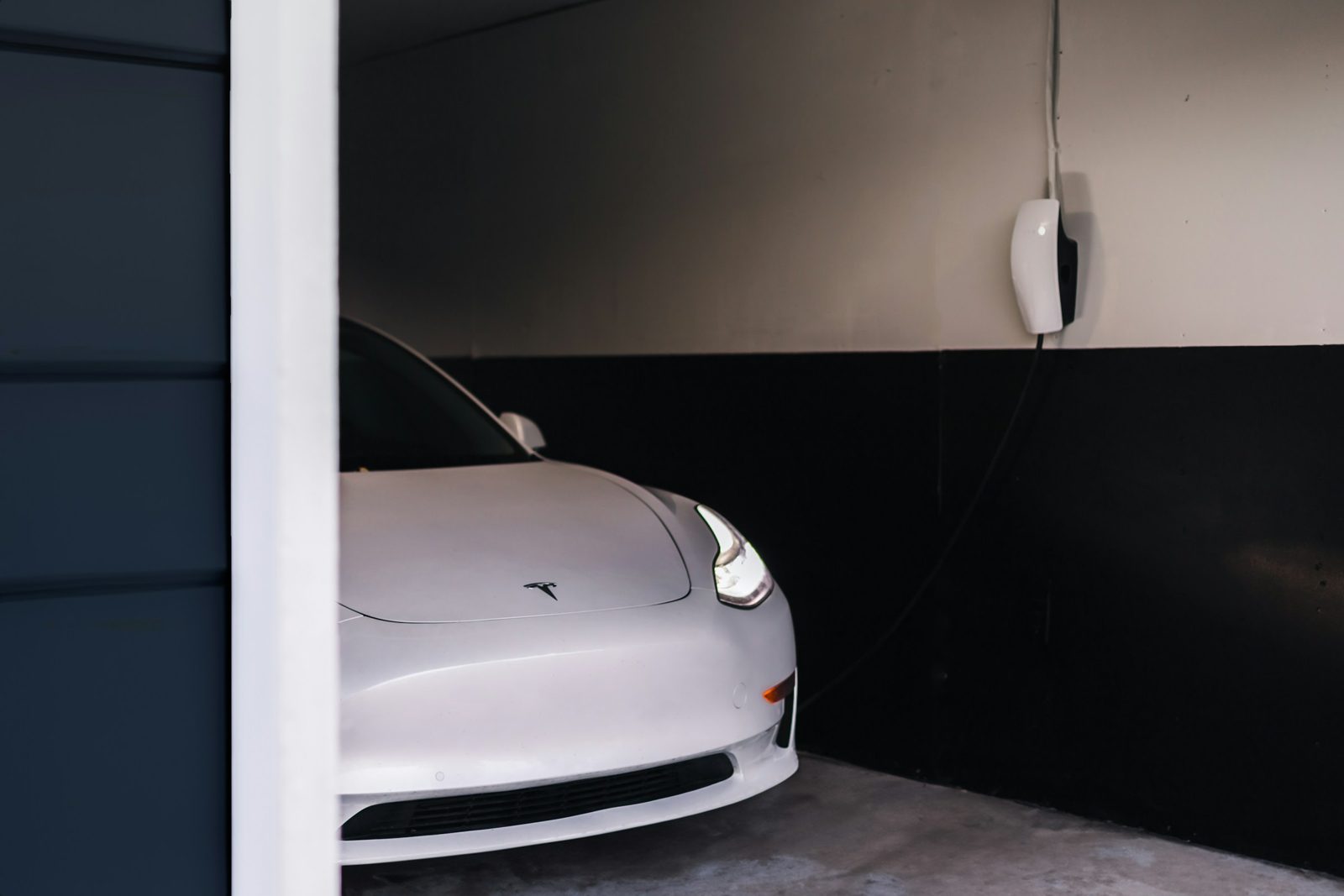 White Tesla parked in a home garage beside a wall-mounted EV charger