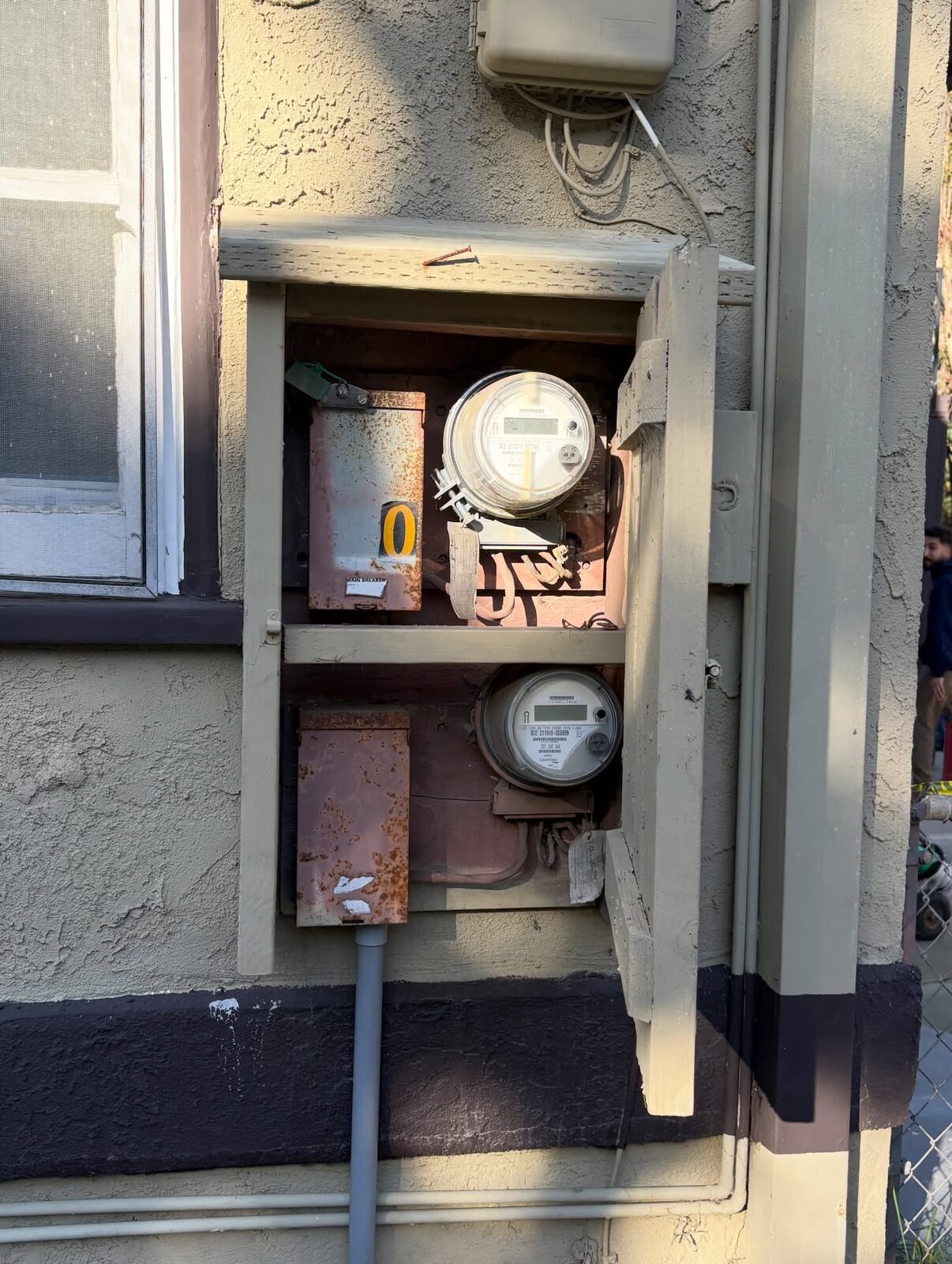 Two utility meters and rusted disconnect boxes in a wooden wall enclosure